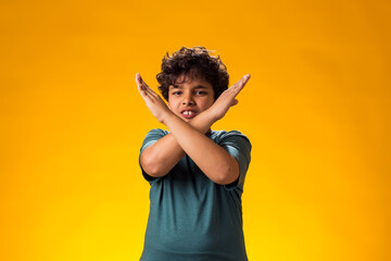 Child boy showing stop gesture on yellow background. Bulling and negative emotions concept