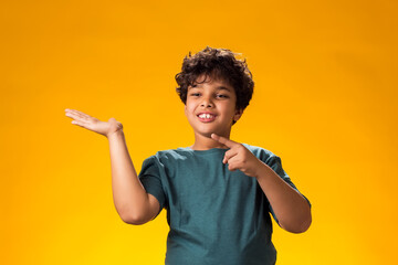 Smiling child boy pointing finger at something over yellow background. Positive emotions concept