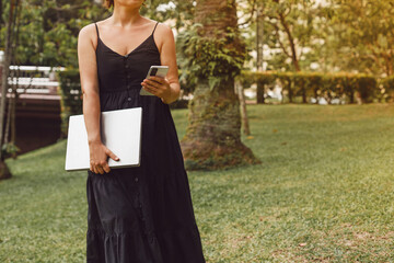 Young woman using phone and laptop in park. Concept of a realtor and the work of a freelancer.