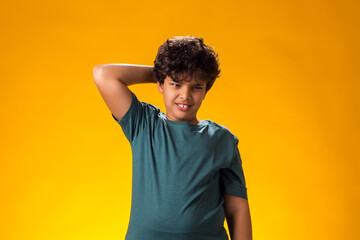 Doubtful kid boy scratching his head over yellow background. Uncertainty concept