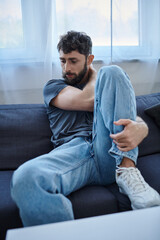 traumatized anxious man in casual clothes sitting on sofa during breakdown, mental health awareness