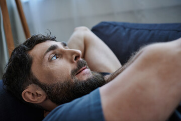 Fototapeta na wymiar depressed bearded man in casual attire lying on sofa during breakdown, mental health awareness