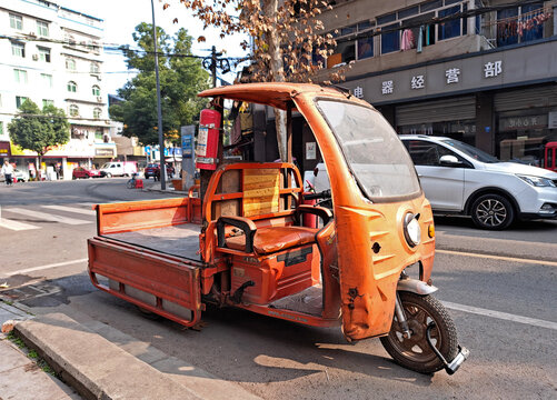 Chengdu, China - 03 January, 2024: Old orange cargo tricycle on street in Chengdu, China. Three-wheeler transport vehicle parked near a sidewalk