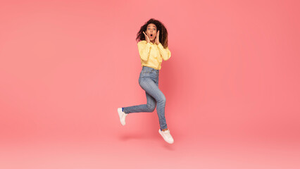 Fototapeta na wymiar Surprised black woman jumps, touches cheeks, excited on pink backdrop