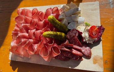 thin slices of speck with salami and goat cheese presented on a wooden board