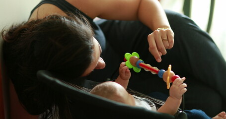 Candid mom interacting with newborn baby playing with toy in chair