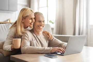 Excited smiling senior spouses using laptop computer at home
