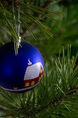 Vibrant blue Christmas bauble with a painted candle nestled among fresh green pine needles, adding whimsy to holiday decor. Hand-painted candle design on a classic holiday decoration.