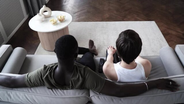 Young afroamerican man and caucasian woman watching TV, aeting chips