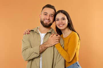 Happy Young Couple Hugging And Holding Hands Over Orange Background