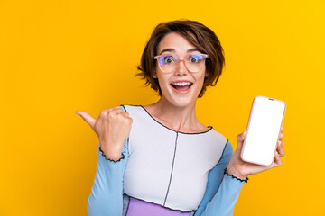Portrait of attractive impressed lady show smart phone screen indicate finger empty space isolated on yellow color background - obrazy, fototapety, plakaty