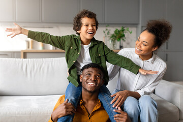 Black boy plays airplane with parents' support at home