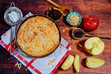 Freshly baked apple pie on a rustic kitchen worktop with ingredients and kitchen utensils.