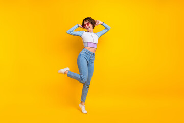 Fototapeta na wymiar Full size portrait of cheerful cute girl enjoy dancing hands touch hair empty space isolated on yellow color background