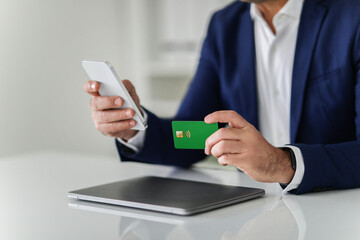 Close-up of a man in a business suit performing a contactless payment with a green credit card