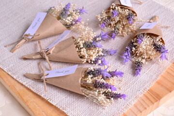 Wedding favours lavender mini bouquet with small flowers, thank you party souvenir original gifts for guests, diy handmade present on rustic favor table witn jute wood background, purple white color
