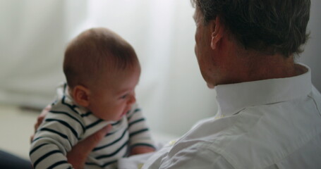 Candid grandfather holding grandson picking up cellphone device with baby