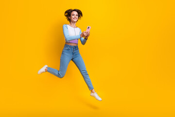 Fototapeta na wymiar Full length portrait of carefree nice person jump hold use smart phone empty space isolated on yellow color background