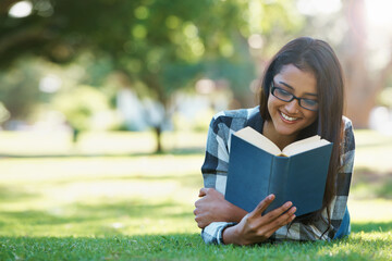 Happy woman, student and reading book in nature for literature, studying or story on green grass. Female person, smart or young adult with smile or glasses for chapter, learning or outdoor education