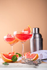 Grapefruit martini cocktail with cold champagne. Refreshing summer cocktail with garnish of a piece of grapefruit and mint on a light background with bar tools and ingredients