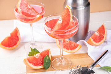 Grapefruit martini cocktail with cold champagne. Refreshing summer cocktail with garnish of a piece of grapefruit and mint on a light background with bar tools and ingredients