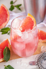 Grapefruit margarita or lemonade cocktail with cold champagne. Refreshing summer cocktail with garnish of a piece of grapefruit and mint on a light background with bar tools and ingredients