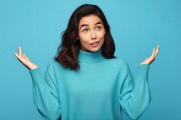 Young woman with arms out, shrugging her shoulders, saying: who cares, so what, I don't know. Isolated studio shot on blue background. Whatever gesture.