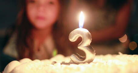 Child blowing candle on birthday cake celebrating three years of age