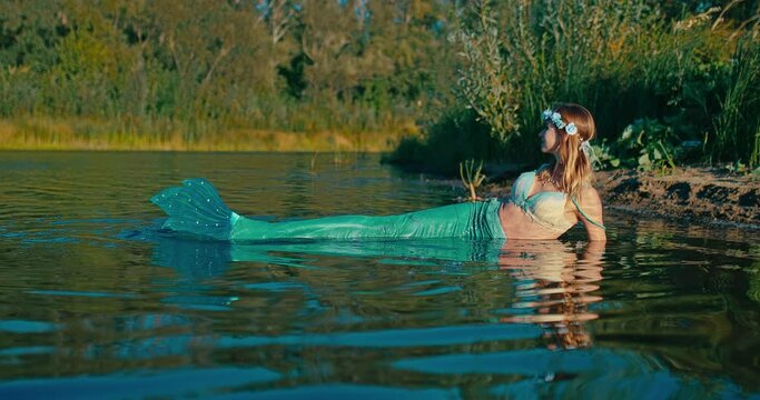 fascinating beautiful rusalka with big fishtail lying on river coast in shallow, portrait 4K, Prores