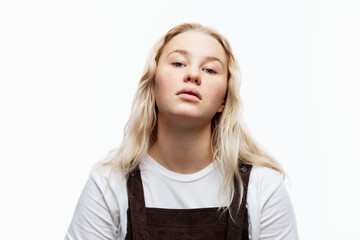 A capricious teenage girl. A cute blonde with freckles in a white T-shirt and brown overalls with...