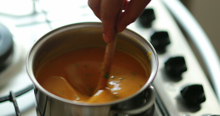 Closeup of hand stirring orange soup
