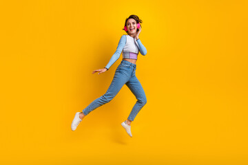 Fototapeta na wymiar Full size portrait of overjoyed girl arm touch headphones jump empty space ad isolated on yellow color background
