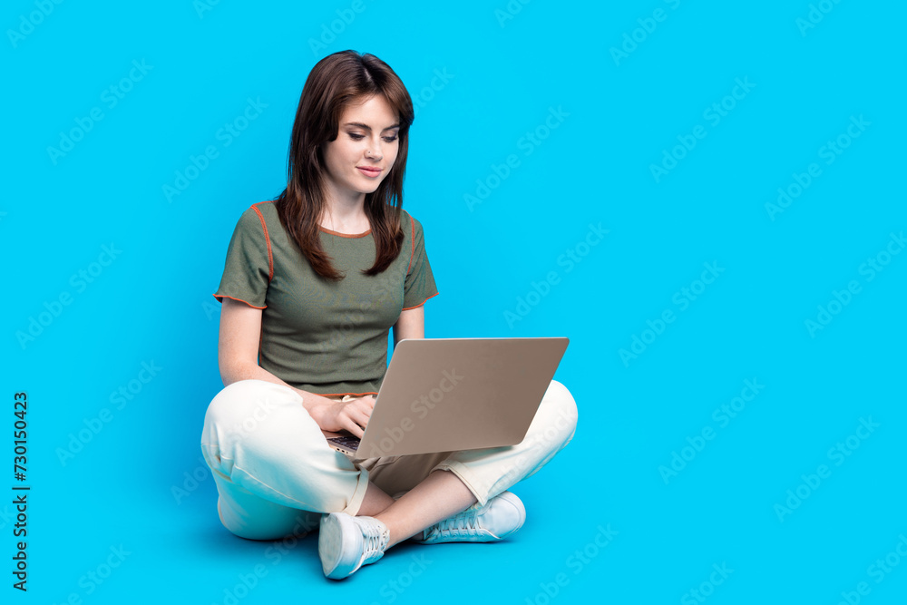 Wall mural Full size photo of focused intelligent woman wear green t-shirt sit on floor typing message on laptop isolated on blue color background