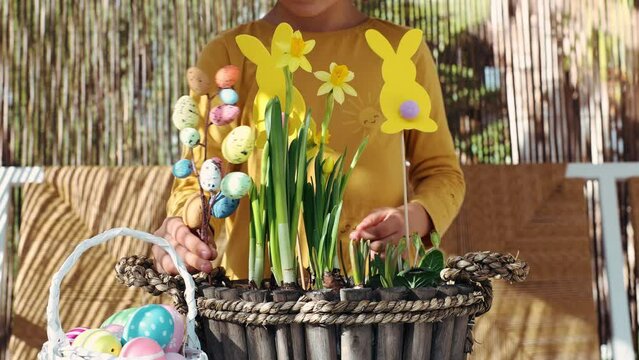 Happy child girl make spring Easter composition with yellow flowers, paper colored Easter bunny, eggs basket. Children prepare decoration present for Easter party at home. Kid creativity and hobby DIY