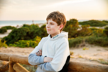 Naklejka na ściany i meble Happy cheerful teenager standing on beach at sunset. happy preteen boy smiling at the camera. Kid on family vacation at the sea.