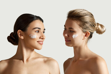 Blonde and brunette beautiful girls with clear, well-kept skin applying face moisturizing cream...
