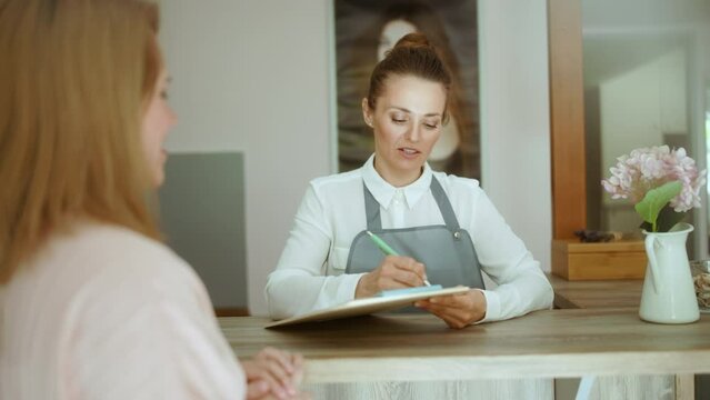 woman hair salon worker in modern hair studio with clipboard and client on reception.
