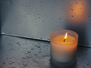 Scented candle on silver surface with water drops, peace and meditation concept.