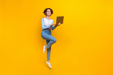 Full size portrait of gorgeous girl jump hold wireless laptop empty space isolated on yellow color...