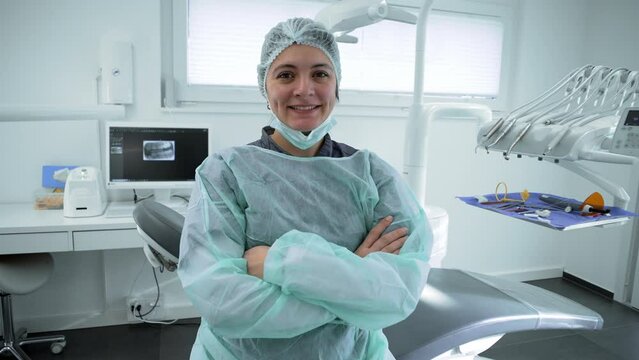 Portrait of a happy female Dentist at dental clinic with arms crossed representing healthcare professional workforce wearing uniform with equipment in background