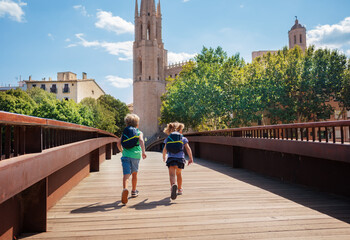 Kids tourists with backpacks run on bridge in Girona town