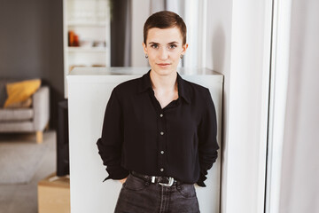 Serious Young Woman in Black Blouse Leaning Against Cabinet in Office