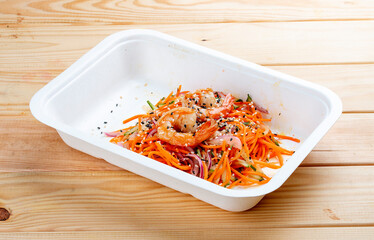 Korean-style salad with shrimp, fresh vegetables and spicy carrots. Healthy food. Takeaway food. On a wooden background.