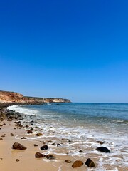 Fototapeta na wymiar Stones at the sandy ocean beach, rocky ocean coast, clear blue sky