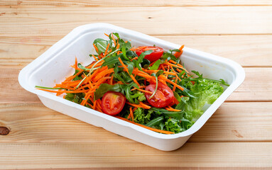 Salad mix (greens, carrots and cherry tomatoes). Healthly food. Takeaway food. On a wooden background.
