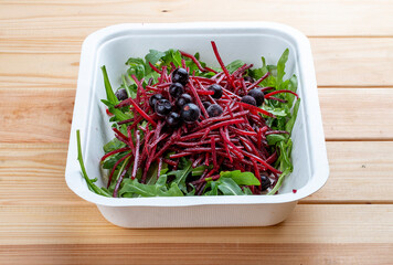 Salad of arugula, beets and berries. Healthly food. Takeaway food. On a wooden background.