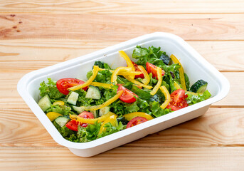 Salad with cucumber, tomatoes and sweet pepper. Healthly food. Takeaway food. On a wooden background.