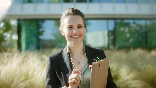 happy modern middle aged woman worker in business district in black jacket with documents and folder.