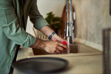 A man washing dishes in the kitchen sink in the kitchen, using a red cleaning sponge.
