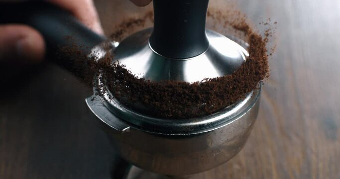 Super slow motion macro of barista preparing espresso with portafilter and tamper with fresh flavorful aromatic roasted ground coffee powder at 1000 fps in cafeteria for serving it to customer.